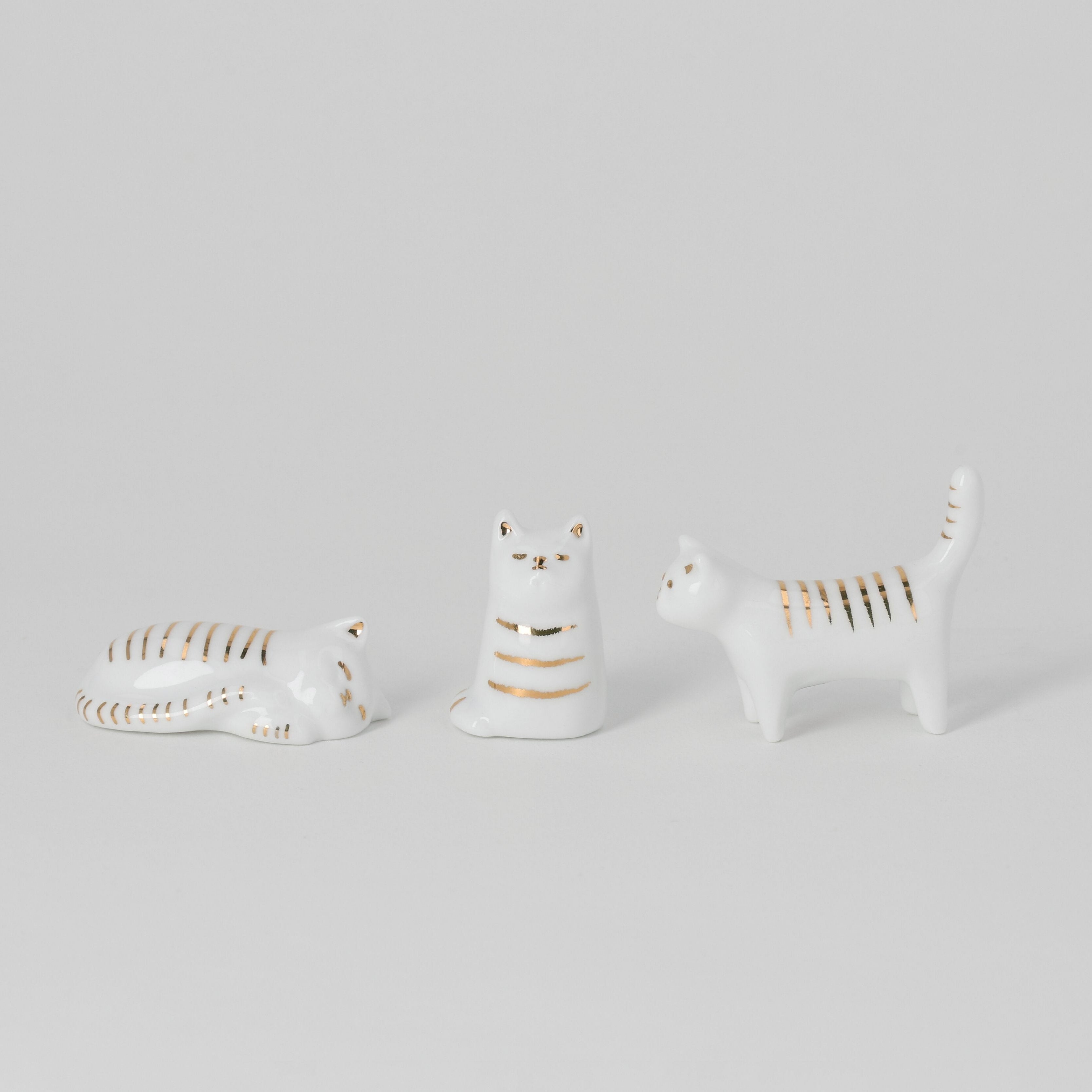 Three ceramic cat figurines on a light gray background