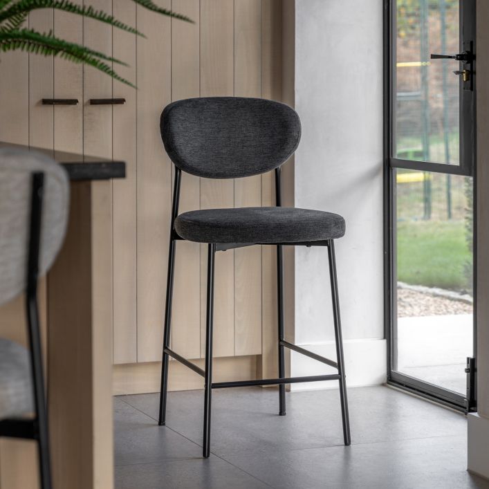 Oppo Stool in dark grey with a cushioned seat and backrest, metal legs, shown in a modern kitchen near a glass door.