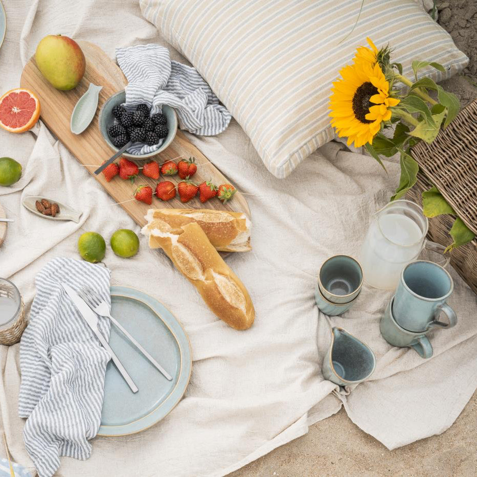 Outdoor picnic setup with food, drinks, and utensils on a blanket