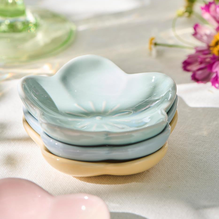 Set of ceramic leaf-shaped dishes in pastel colors on a light surface with flowers in the background.