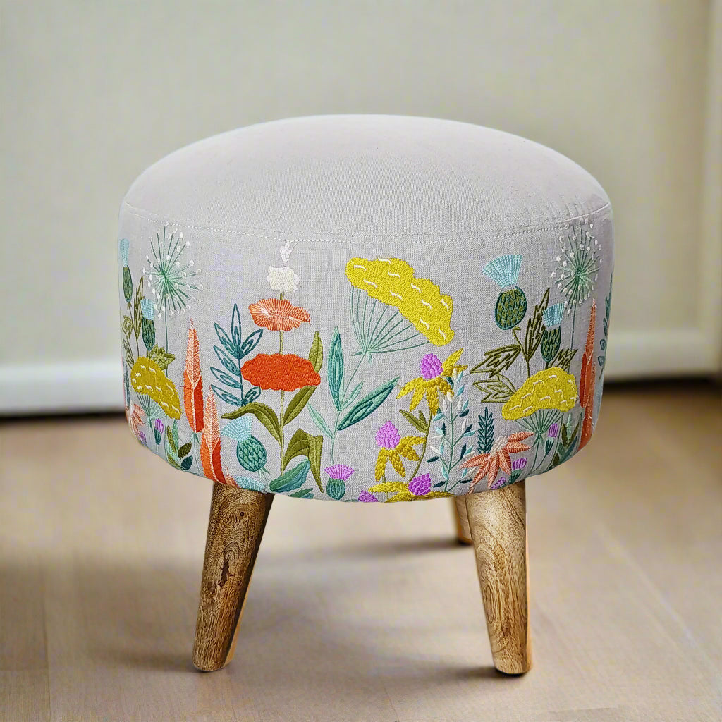 Small stool with floral embroidery and wooden legs on a neutral background