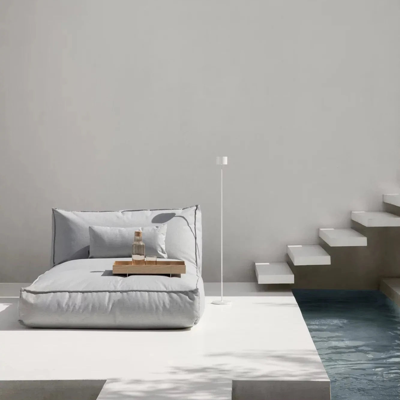 Modern bedroom with a bed, nightstands, and a lamp against a plain wall.