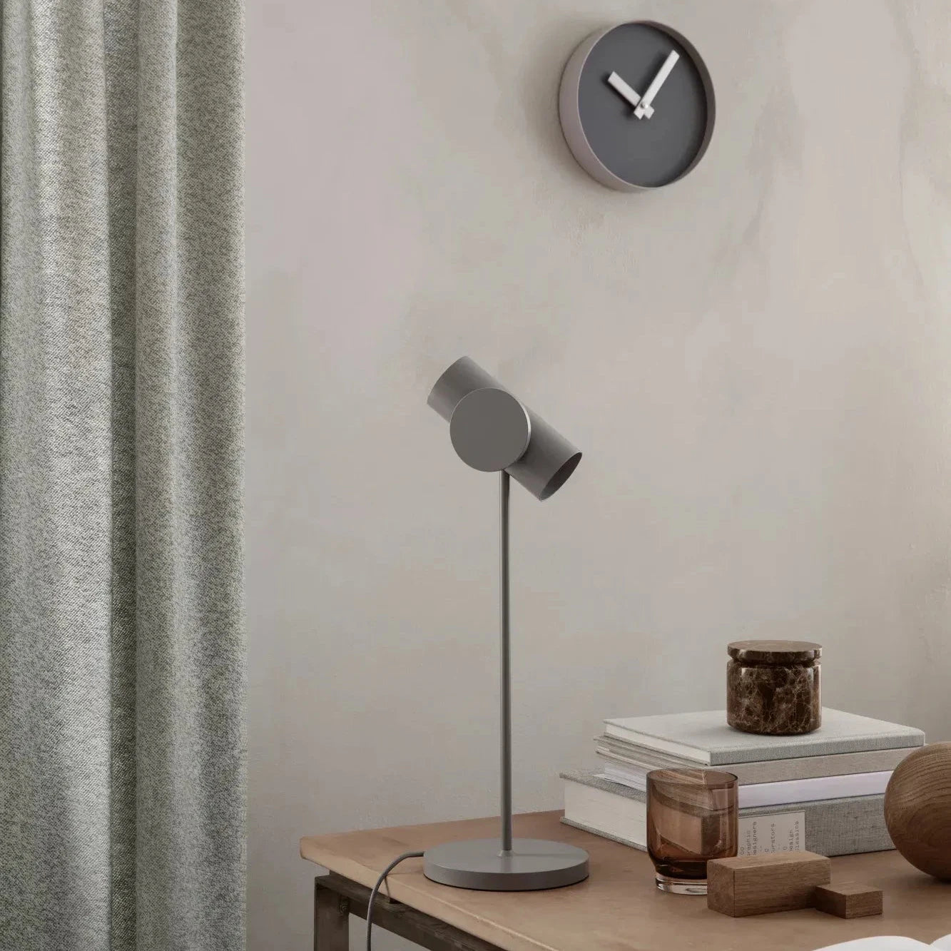 Modern interior with a wall clock, table lamp, and books on a wooden surface.