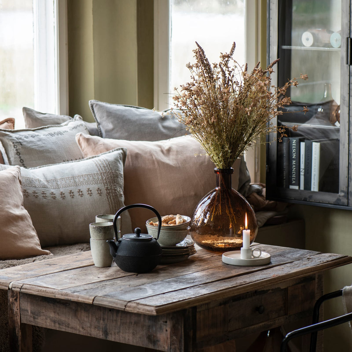 Ib Laursen linen cushions in neutral shades on a sofa beside a rustic coffee table and dried flowers