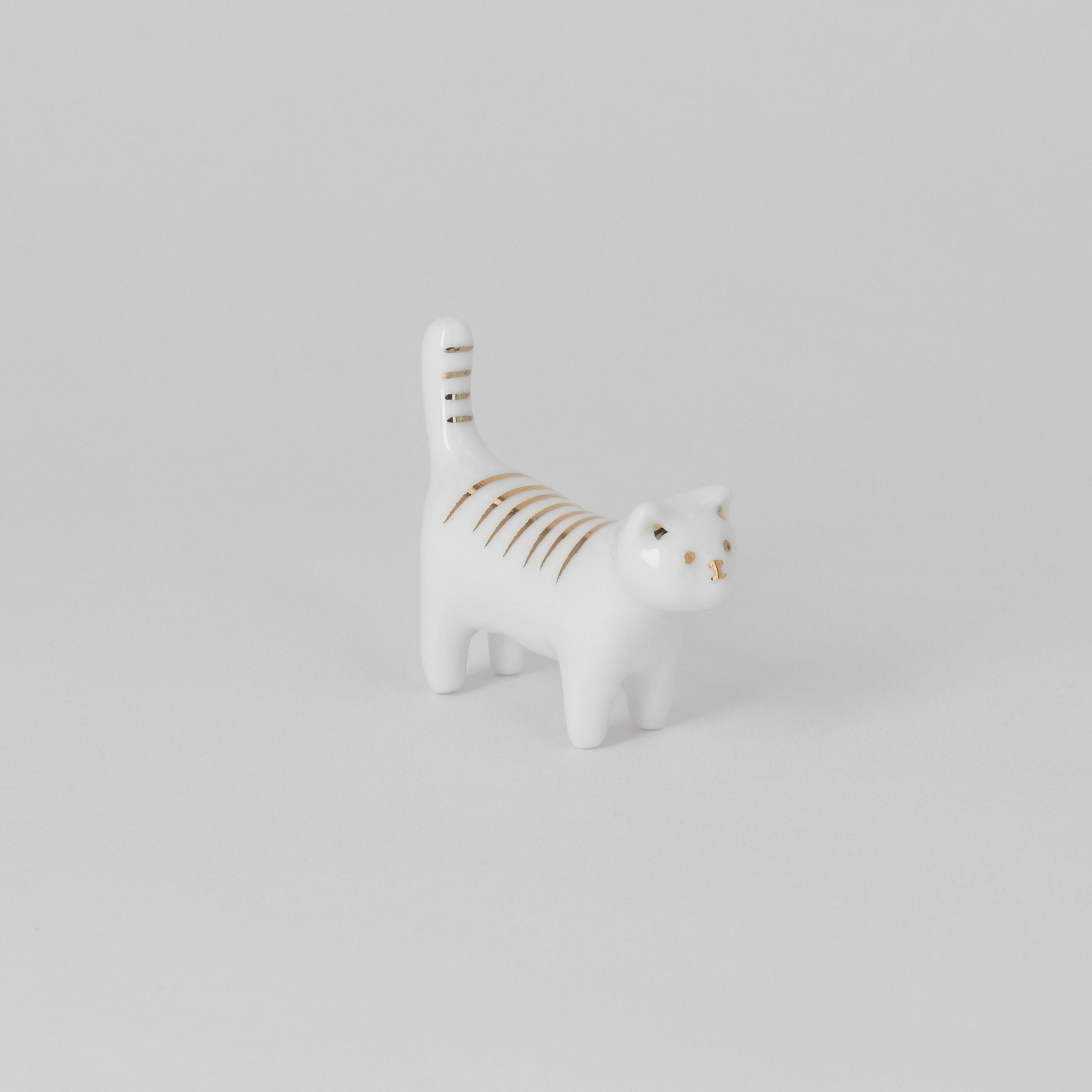 White ceramic cat figurine with gold stripes on a light gray background