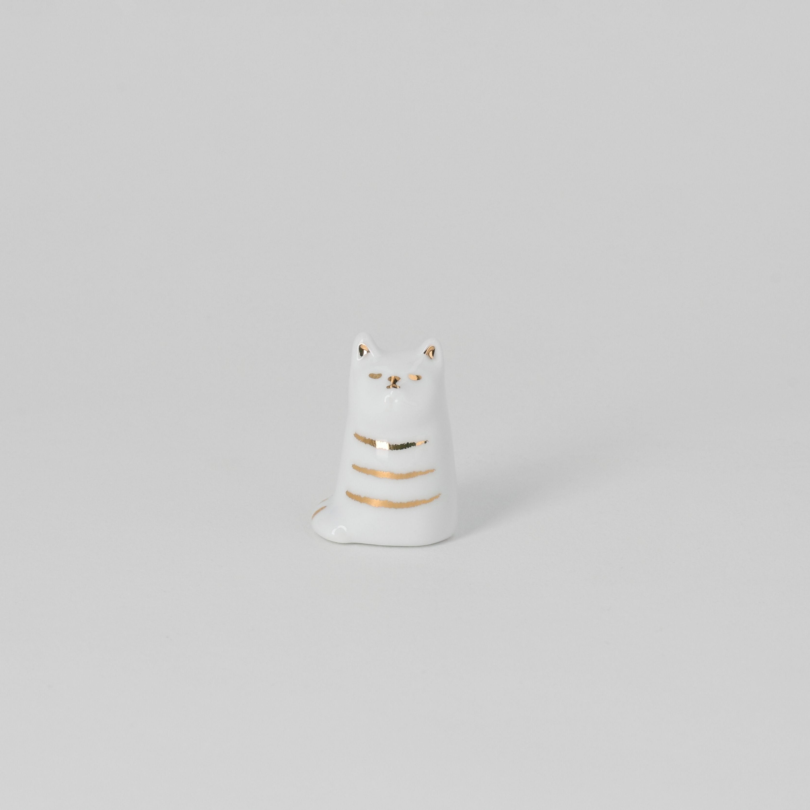 White ceramic cat-shaped object with gold accents on a light gray background