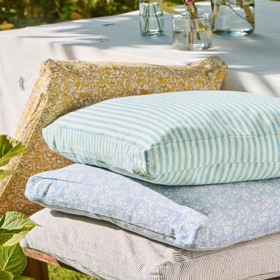 Stack of outdoor cushions on a wooden bench with a garden background
