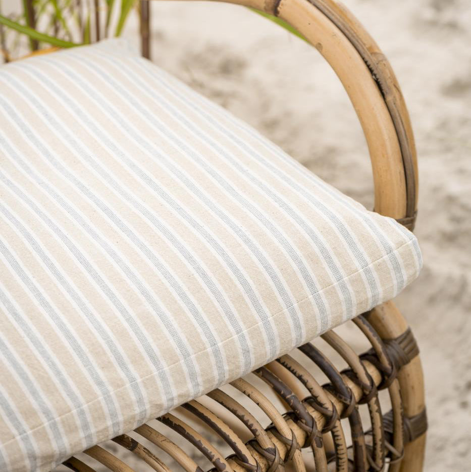 Wicker chair with a striped cushion on a sandy background