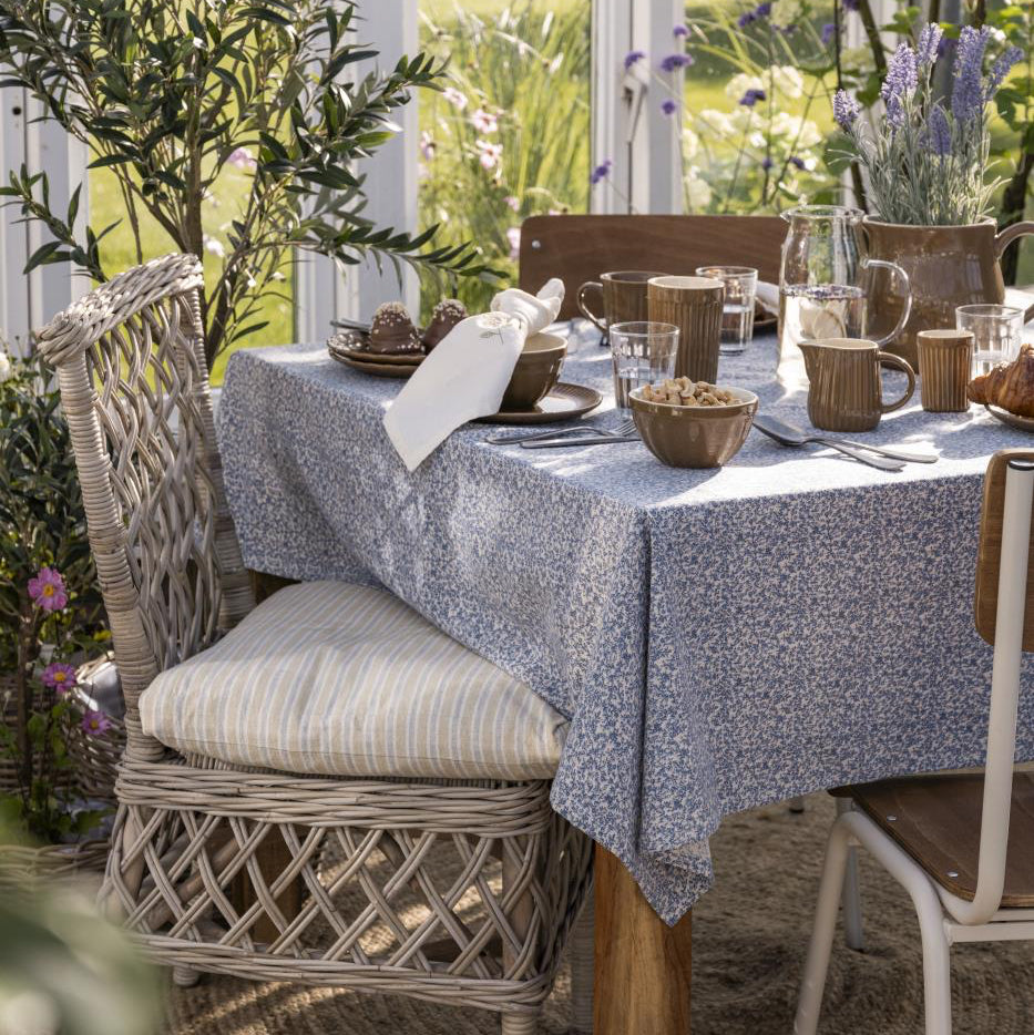 Dining table set with a textured tablecloth in an outdoor setting with chairs and decorative elements.