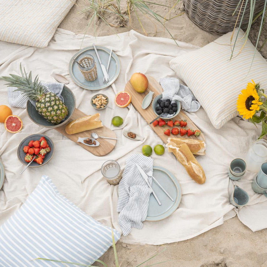 Picnic setup on a blanket with food and drinks on a sandy surface