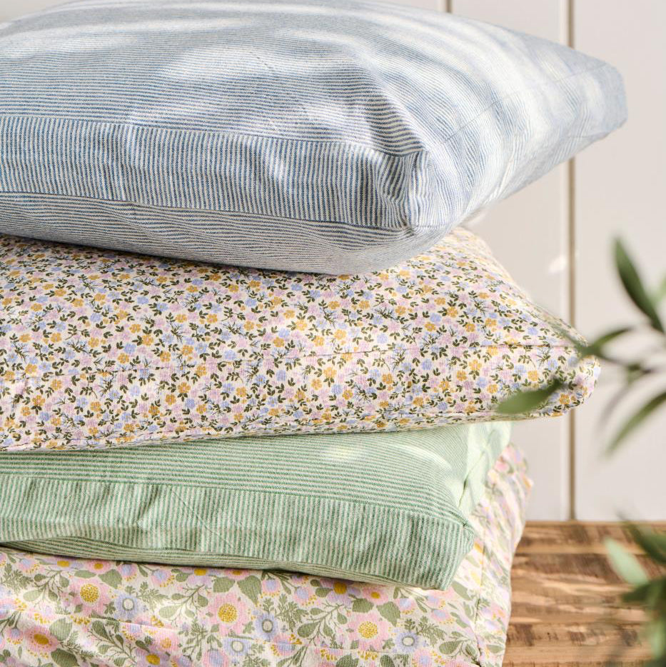Stack of floral and striped pillows on a wooden surface with a white paneled background