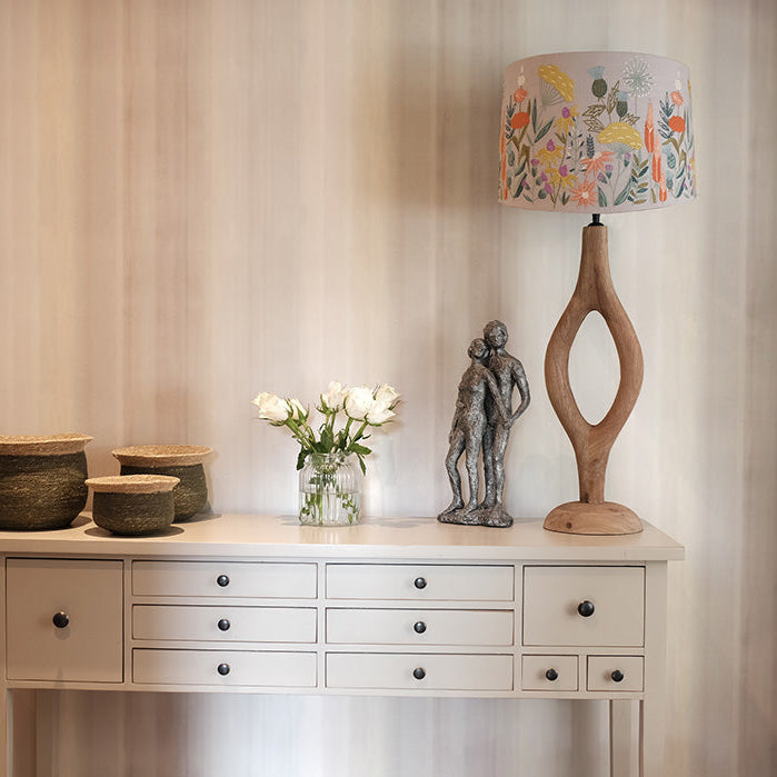 Decorative table with a lamp, flowers, and sculptures against a neutral wall.
