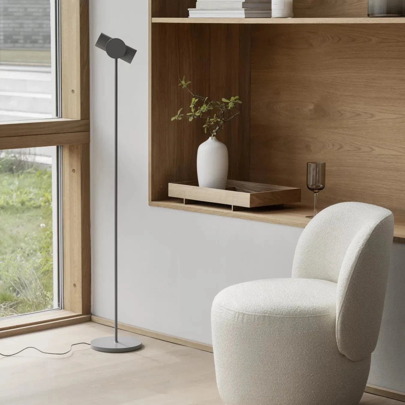 Modern interior with a white chair, floor lamp, and wooden shelves.
