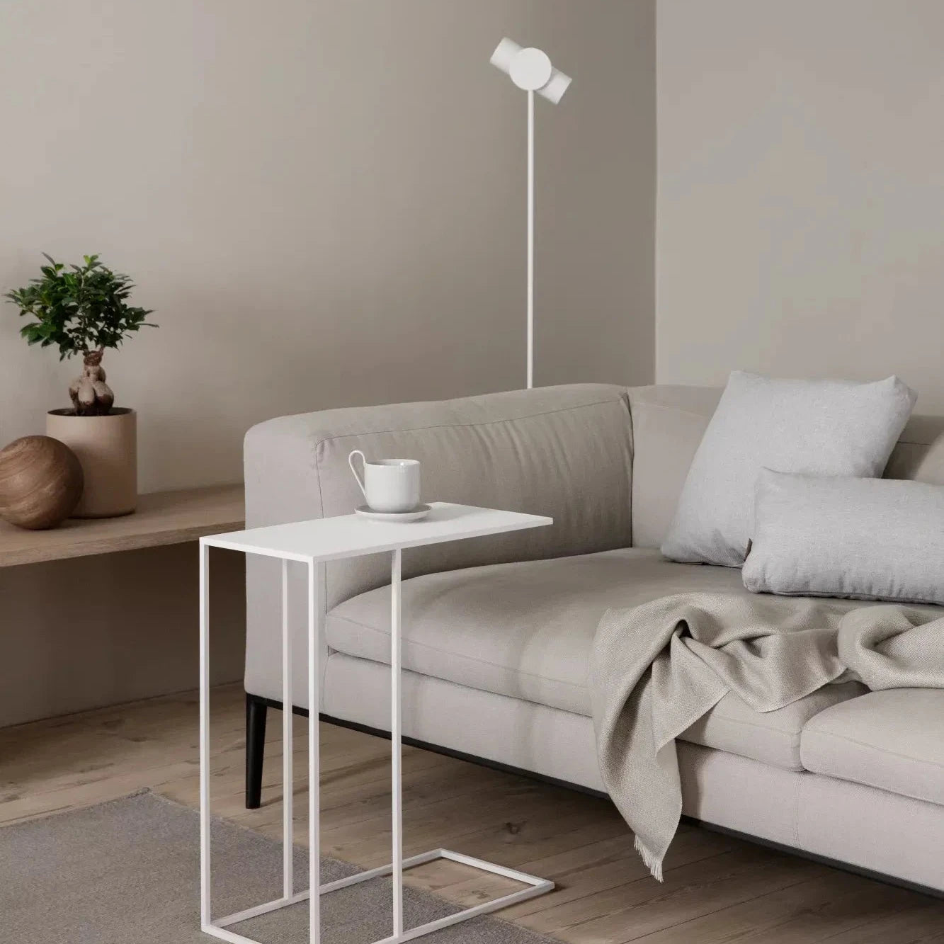 Modern living room with a beige sofa, side table, and floor lamp against a neutral wall.
