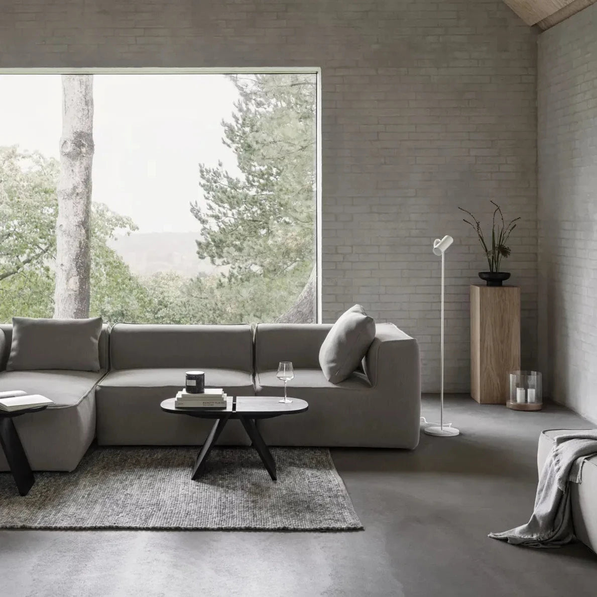 Modern living room with a gray sectional sofa, coffee table, and large window view.