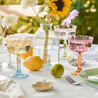 Outdoor table setting with floral arrangements, glasses, and fruits on a white tablecloth.