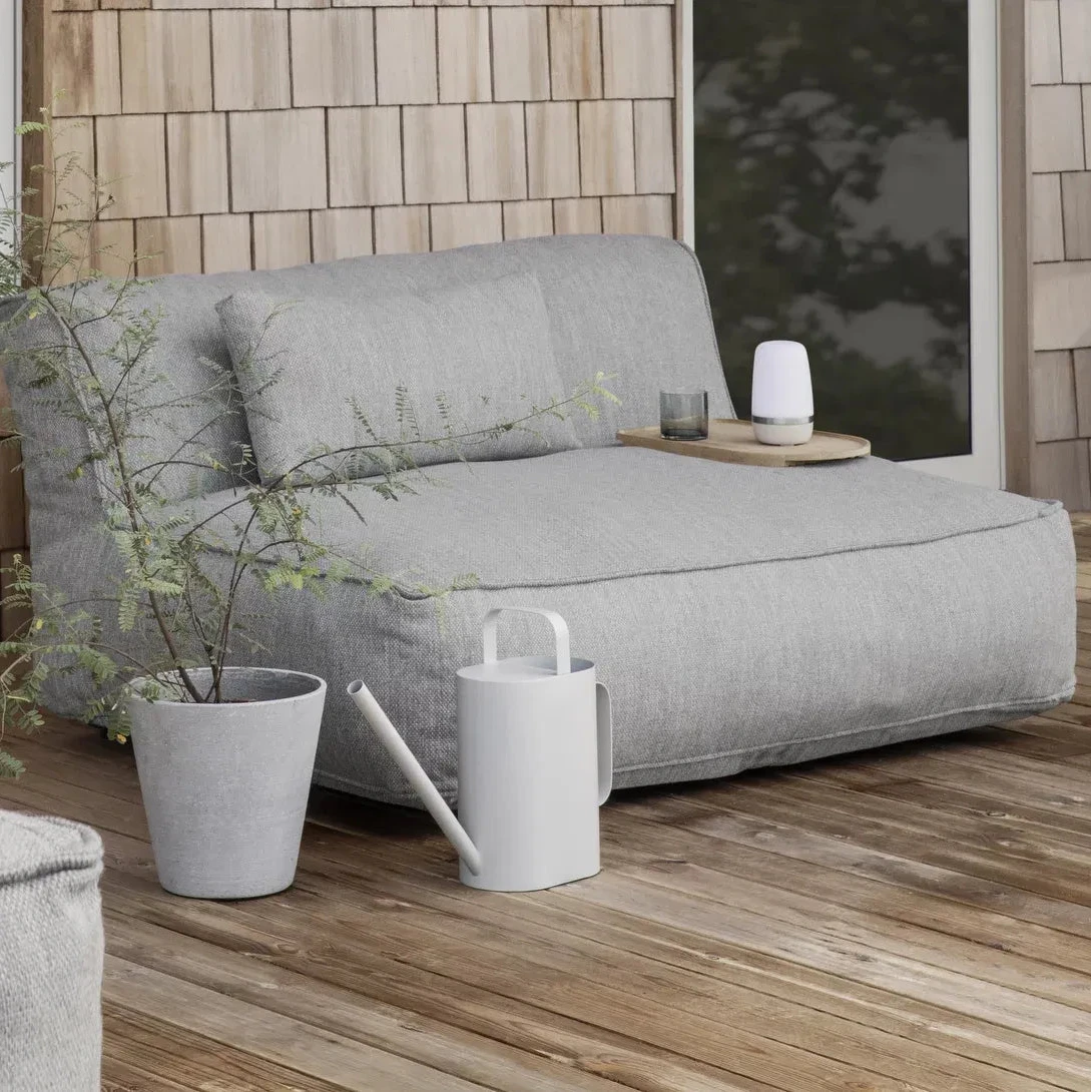 Gray outdoor sofa with a plant and watering can on a wooden deck.