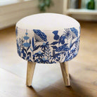 A round footstool with blue floral embroidery on a beige background, featuring a flat base with three wooden legs.
