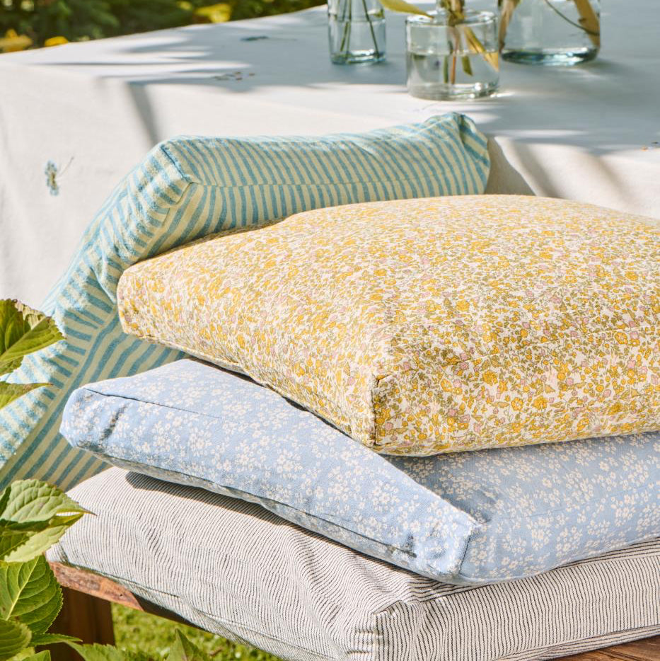 Stack of colorful cushions on a wooden bench with a garden background