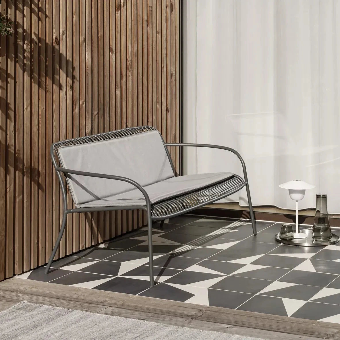 Outdoor chair with gray cushions on a patio with geometric tile flooring.