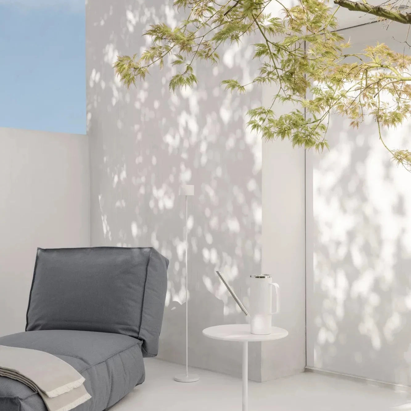 Modern outdoor setting with a gray chair, white table, and tree shadows on a white wall.