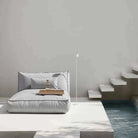 Modern bedroom with a bed, nightstands, and a lamp against a plain wall.