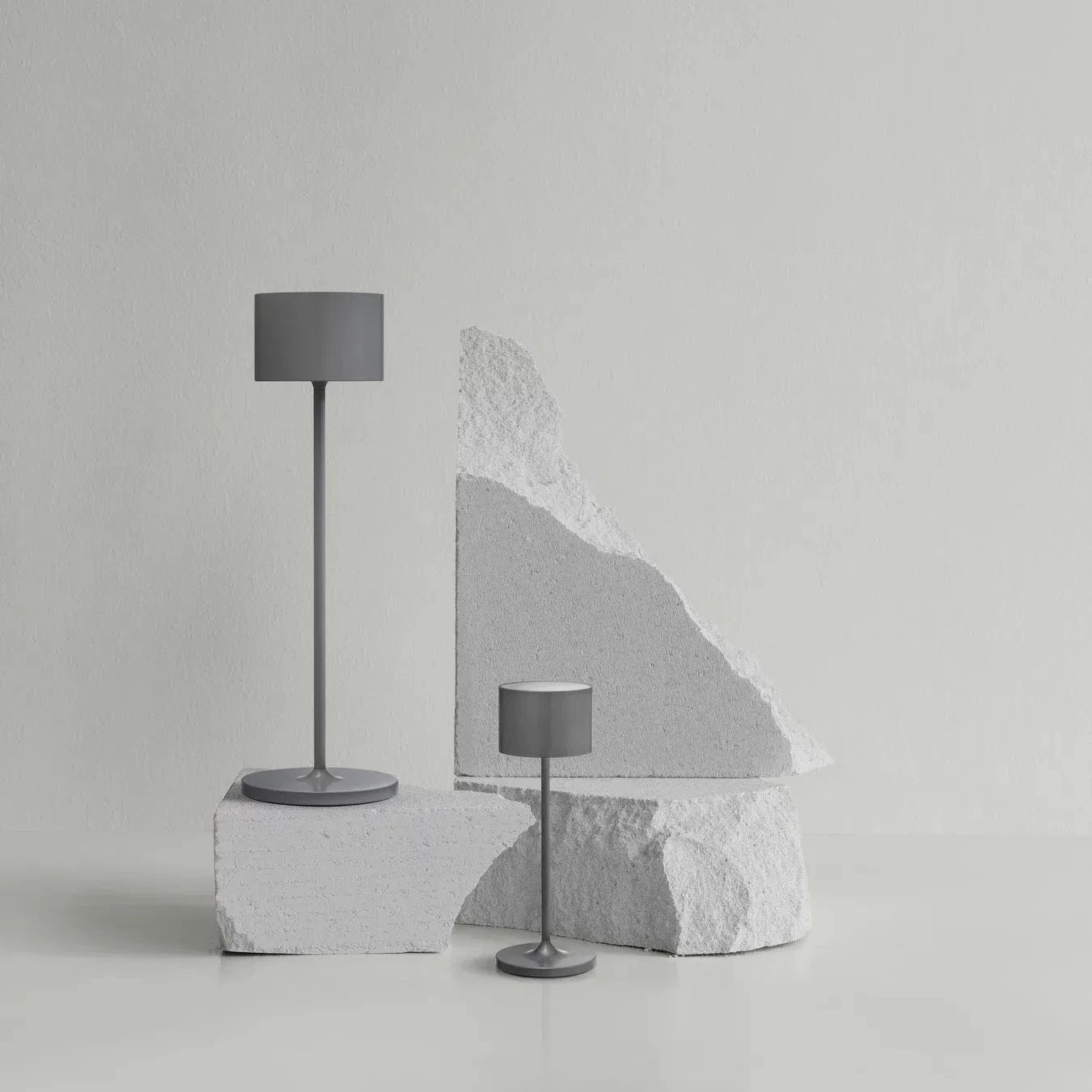 Two gray floor lamps on a light gray background with a large stone block.