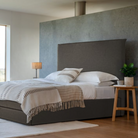Double bed with bed frame in smoke color featuring a tall upholstered headboard, set against a modern gray wall backdrop.