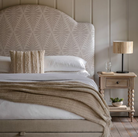 Tadley 4'6 bed with a patterned headboard, neutral bedding, and a wooden bedside table featuring a lamp and decor.