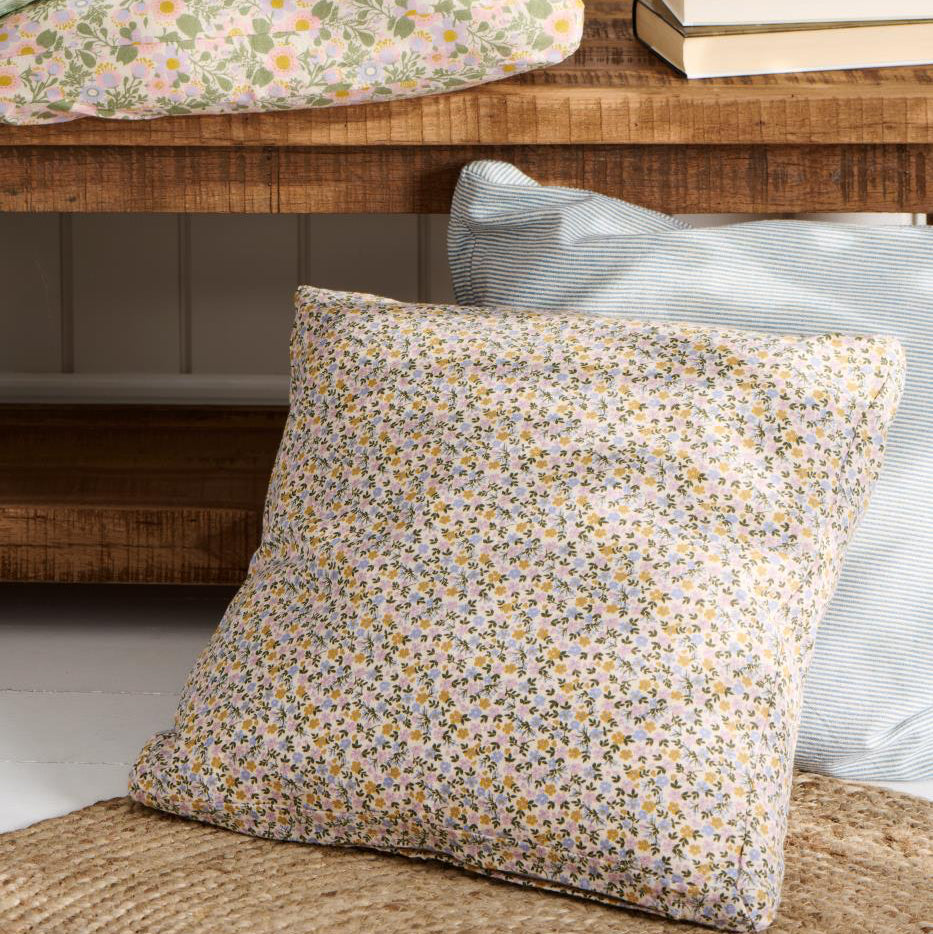 Floral-patterned pillow on a wooden bench with a neutral background