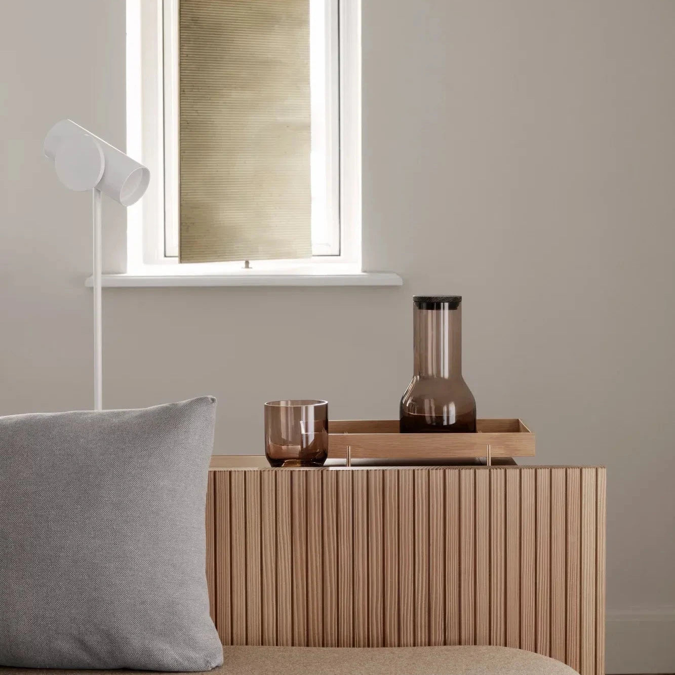 Minimalist bedroom with wooden nightstand, gray pillow, and lamp.