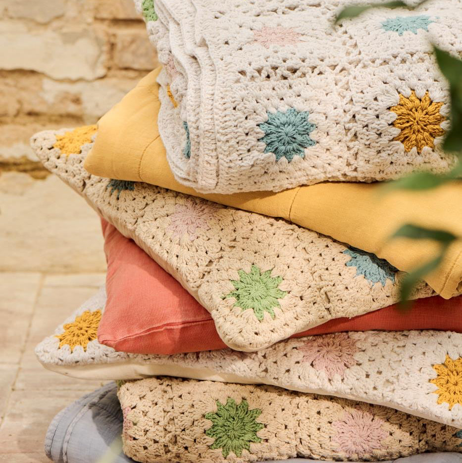 Stack of colorful crocheted blankets with floral patterns on a wooden surface.