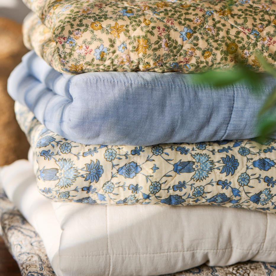 Stack of folded floral and solid-colored blankets on a wooden surface