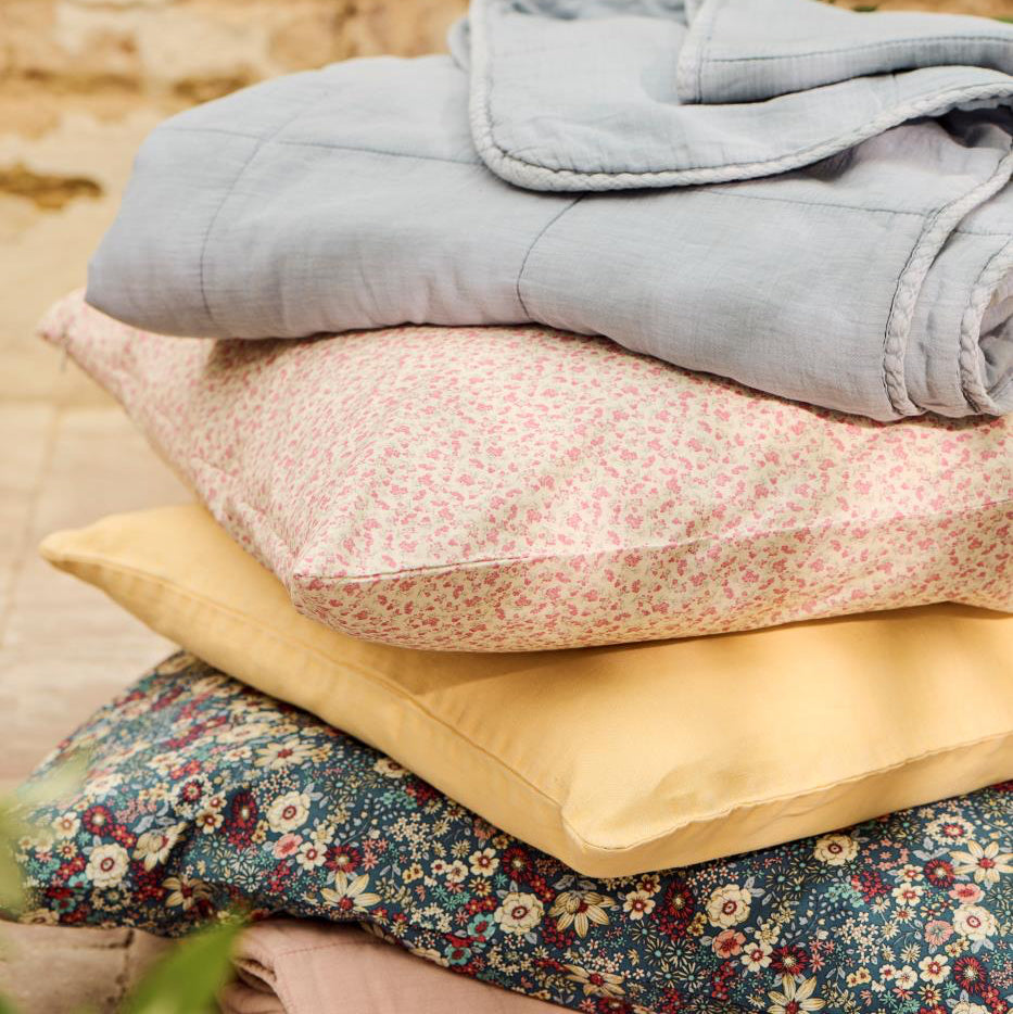 Stack of various fabrics including floral, solid, and textured patterns on a wooden surface.