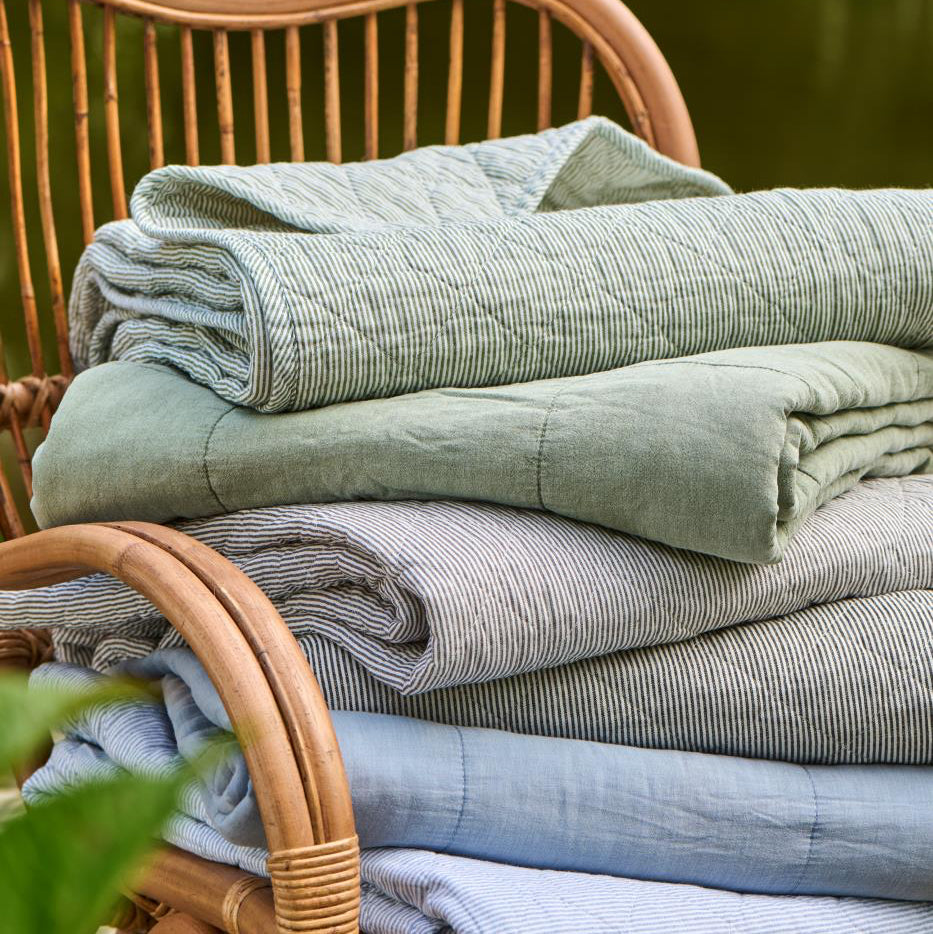 Stack of folded fabric sheets in various shades of green and blue on a wicker chair.