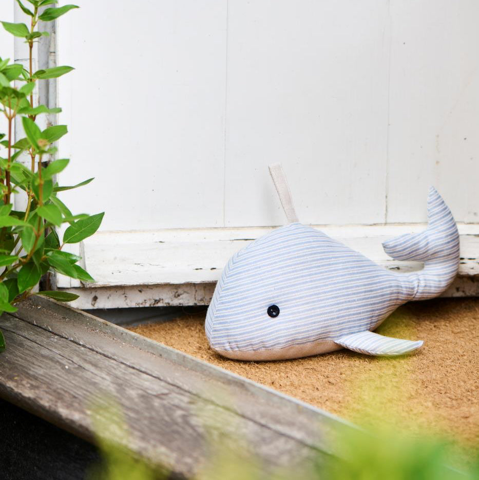 White whale plush toy on a wooden surface with a white wall and green plant in the background