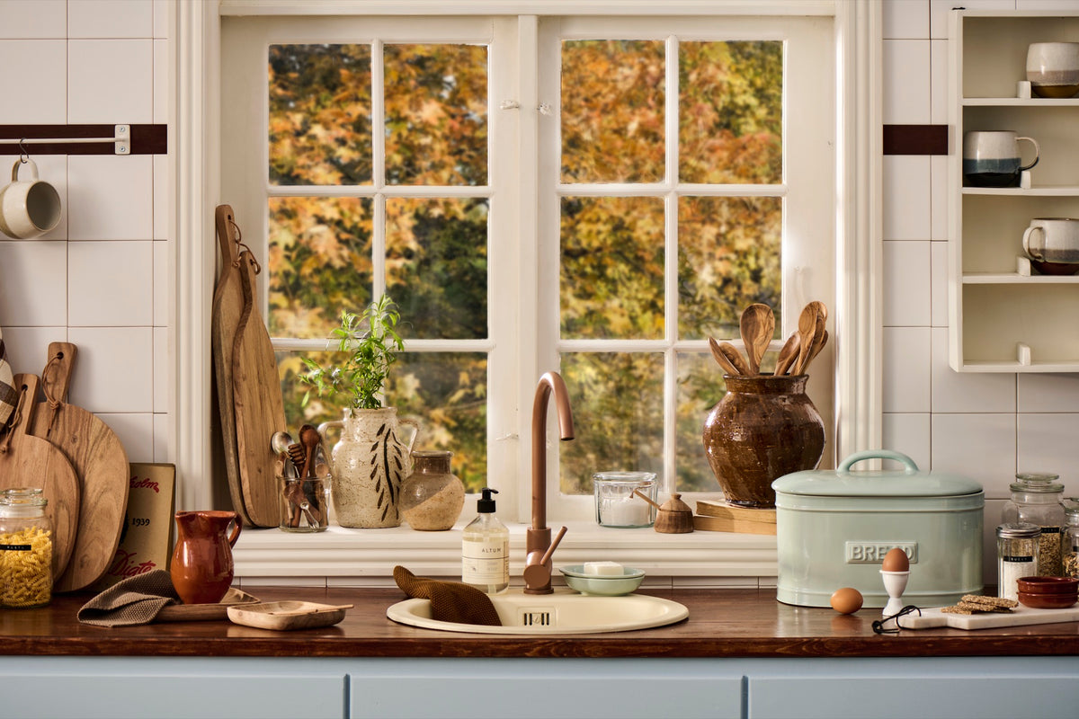 Ib Laursen autumn kitchen with olivewood utensils, rustic ceramics and a sage bread bin beside a window overlooking golden leaves