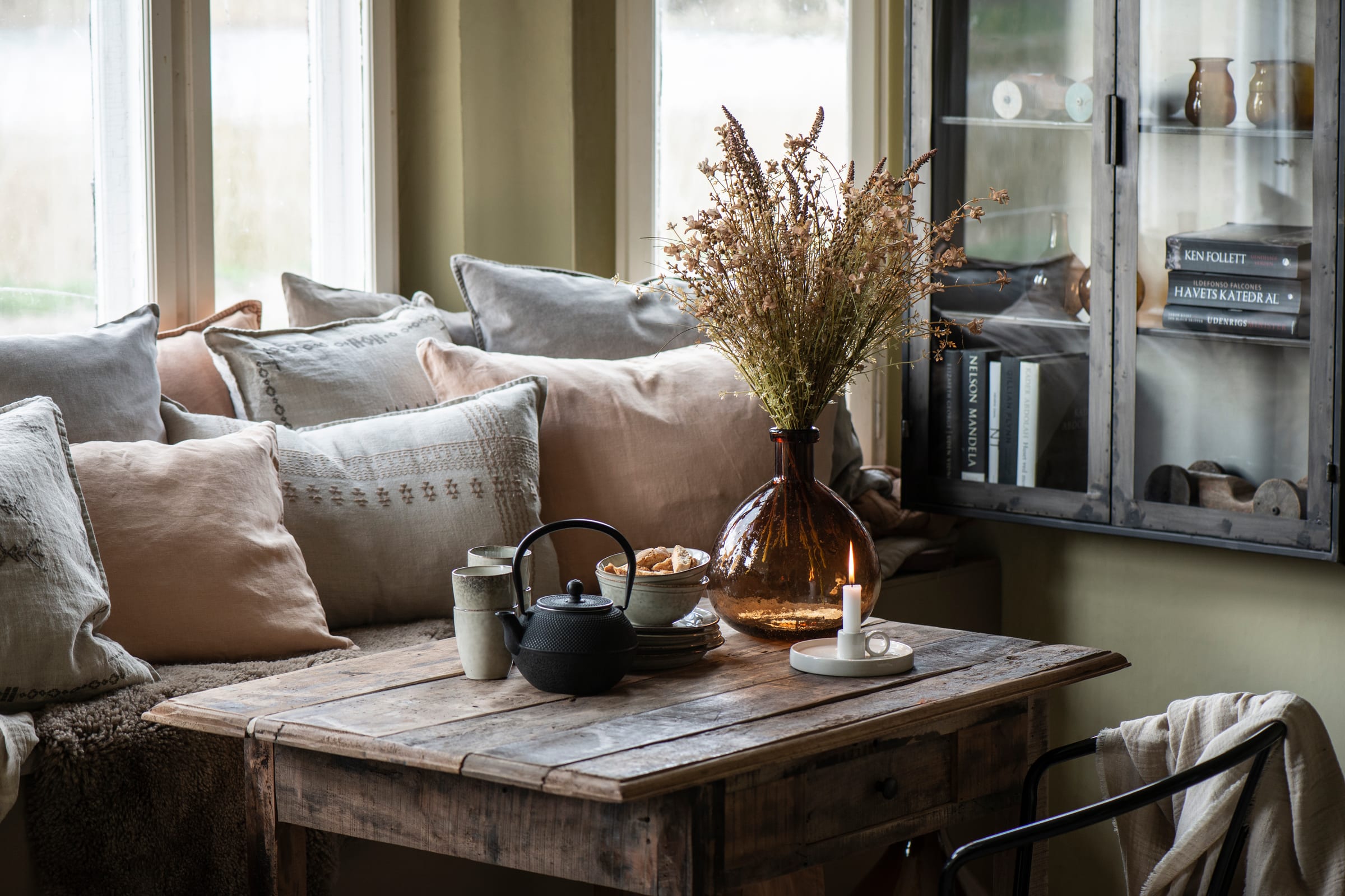 Ib Laursen linen cushions in neutral shades on a sofa beside a rustic coffee table and dried flowers